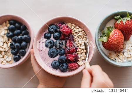 Smoothie bowl with yogurt blueberry raspberry oat grain strawberry healthy breakfast fresh fruit closeup hand holding spoon delicious and nutritious meal 131540414
