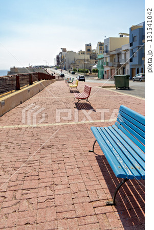 Xghajra Malta seaside promenade with blue bench and coastal town view 131541042