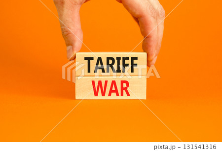 Trade tariff war symbol. Concept word Tariff war on beautiful wooden blocks. Beautiful orange paper background. Businessman's hand. Business trade tariff wars concept. Copy space. Trade tariff war symbol. Concept word Tariff war on beautiful wooden blocks. Beautiful orange paper background. Businessman's hand. Business trade tariff wars concept. Copy space. 131541316