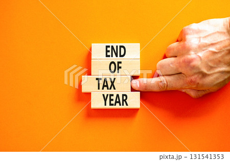 End of tax year symbol. Concept words phrase End of tax year on beautiful wooden blocks. Beautiful orange paper background. Businessman's hand. Business End of tax year concept. Copy space. 131541353
