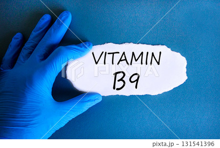 Vitamin B9 folic acid symbol. Concept words Vitamin B9 on beautiful white paper. Doctor's hand in blue medical glove. Beautiful blue background. Medical healthy lifestyle Vitamin B9 concept. Vitamin B9 folic acid symbol. Concept words Vitamin B9 on beautiful white paper. Doctor's hand in blue medical glove. Beautiful blue background. Medical healthy lifestyle Vitamin B9 concept. 131541396