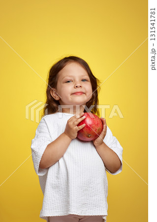 cute little child girl holding a pomegranate on yellow background. 131541781
