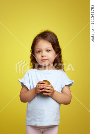 cute Caucasian little child girl holding kiwi fruit on yellow background 131541798