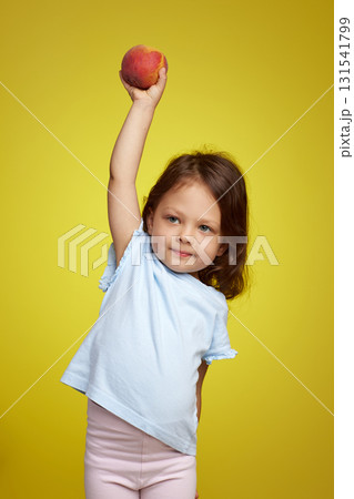 Portrait of brunette little child girl with peach on yellow background 131541799