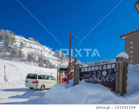 快晴のスキー場麓にある温泉地の案内看板と雪道 (長野県、山ノ内町) 131542334