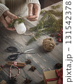 Female hands making Christmas decoration with candle, spruce needles, jute twine on a wooden background, vertical image. 131542378