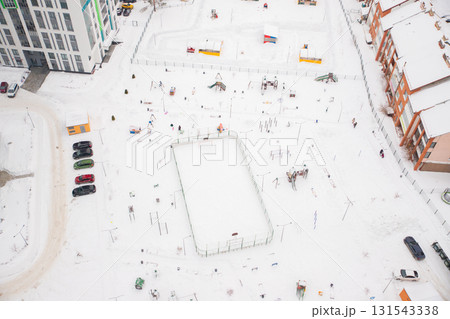 Aerial view of a snow covered playground and parking lot during winter in a residential neighborhood with scattered vehicles 131543338
