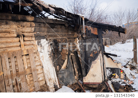 A wooden building shows severe fire damage, with charred walls and a collapsing roof, surrounded by snow. Icicles hang from the remnants, a cold winter day A wooden building shows severe fire damage, with charred walls and a collapsing roof, surrounded by snow. Icicles hang from the remnants, a cold winter day 131543340