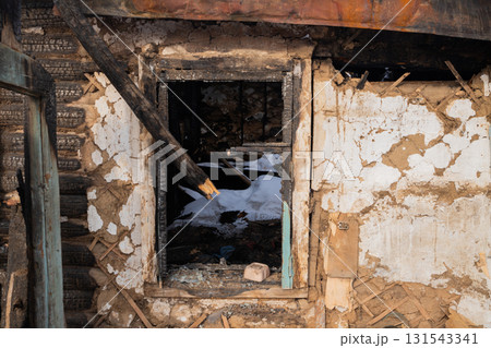 A charred window frame reveals the inside of a burned building, showcasing debris and remnants of a recent fire in an abandoned location. 131543341