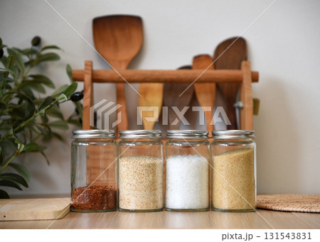 A clear jar that holds seasonings for cooking inside. On the wooden table in the kitchen There are cooking equipment in the background. 131543831