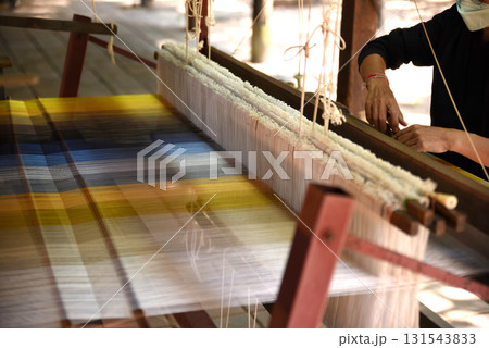 Women's hands weaving silk on a traditional wooden loom. 131543833