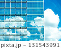 Glass office facade reflects blue sky and cumulus clouds, merging city and nature. 131543991