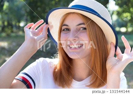 Portrait of happy smiling girl with red hair and in yellow hat outdoors in summer park. Portrait of happy smiling girl with red hair and in yellow hat outdoors in summer park. 131544144