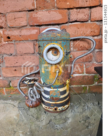 A creative ashtray made from various spare parts and a gas cylinder stands against a red brick wall. A creative ashtray made from various spare parts and a gas cylinder stands against a red brick wall. 131544915