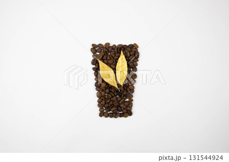 Two golden leaves on coffee beans arranged in the shape of a glass on a white background. Harvesting concept. Two golden leaves on coffee beans arranged in the shape of a glass on a white background. Harvesting concept. 131544924