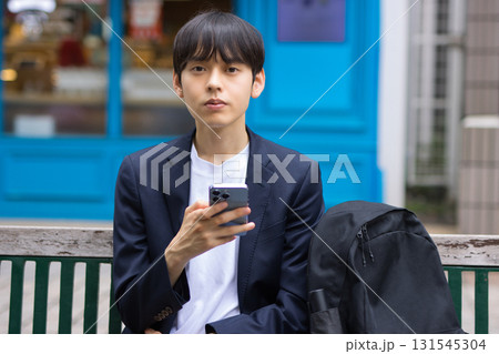 ベンチに座ってスマホを見る20代男性のビジネスマン 131545304