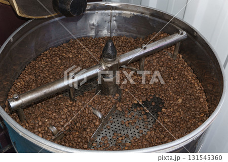 Professional coffee roasting machine with freshly roasted beans during commercial coffee production process in roastery 131545360