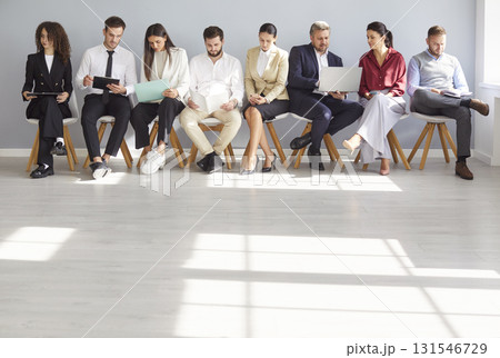 Young office people sits in queue waiting for job interview holding computer devices using internet  131546729