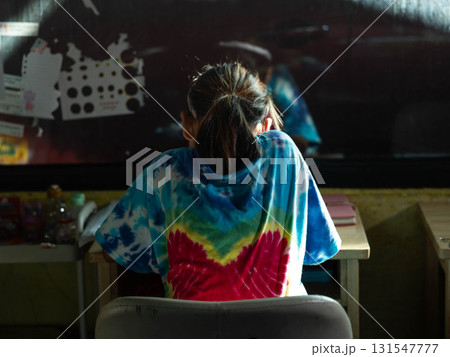 Schoolgirl sitting at desk in colorful tie dye shirt Schoolgirl sitting at desk in colorful tie dye shirt 131547777