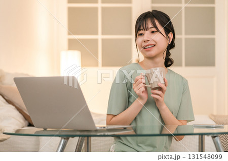 夜の自宅でホットドリンクを飲みながらリラックスしてパソコンを見る若いアジア人女性 夜の自宅でホットドリンクを飲みながらリラックスしてパソコンを見る若いアジア人女性 131548099