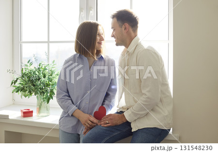 Happy smiling young couple holding red paper heart, celebrating Valentine Day in romantic atmosphere Happy smiling young couple holding red paper heart, celebrating Valentine Day in romantic atmosphere 131548230
