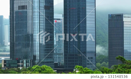 Urban skyline rising behind swaying green trees, merging natural landscape with contemporary architectural silhouettes, representing city environmental balance Urban skyline rising behind swaying green trees, merging natural landscape with contemporary architectural silhouettes, representing city environmental balance 131548536