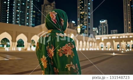 Peaceful Muslim woman in green hijab standing near illuminated mosque, glowing skyscrapers creating serene nighttime urban landscape behind her Peaceful Muslim woman in green hijab standing near illuminated mosque, glowing skyscrapers creating serene nighttime urban landscape behind her 131548723