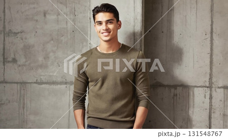 Confident young male model wearing gray casual sweater, smiling brightly during professional studio photoshoot with minimalist concrete wall backdrop 131548767