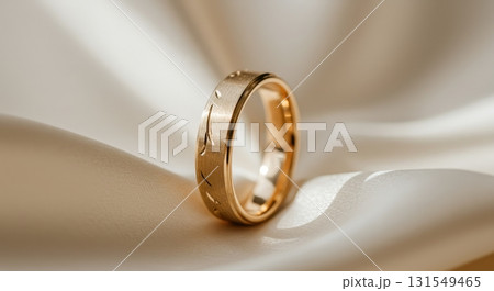 Elegant gold wedding band with engraved pattern resting on a soft satin fabric Elegant gold wedding band with engraved pattern resting on a soft satin fabric 131549465