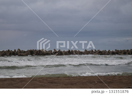 砂浜の海岸と波の打ち寄せる波打ち際とテトラポットの波除と海と雲の多い空の風景 131551876