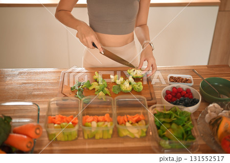Closeup woman chopping broccoli and dividing food into meals weekend meal prep for weight loss Closeup woman chopping broccoli and dividing food into meals weekend meal prep for weight loss 131552517