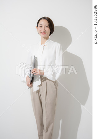 白背景でパソコンを持つオフィスカジュアル、ブラウスで立つカメラ目線の美人な女性 白背景でパソコンを持つオフィスカジュアル、ブラウスで立つカメラ目線の美人な女性 131552996