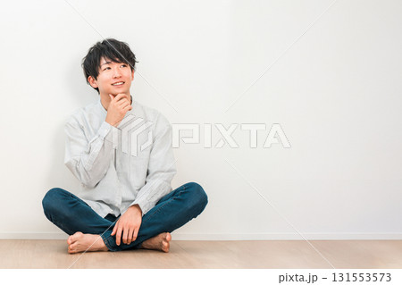 白い壁のリビングにあぐらで座る若いアジア人男性（想像,夢,考える,構想,プラン） 131553573