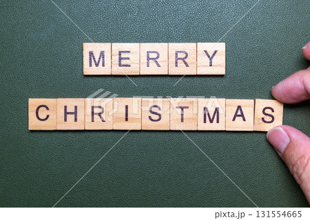 Hands arranging wooden letter blocks spelling Merry Christmas on green background 131554665