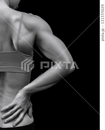 Bodybuilder woman suffers from pain in her back after workout, black background Bodybuilder woman suffers from pain in her back after workout, black background 131555029