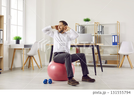 Funny young business man doing sport exercises sitting on fit ball in office. Funny young business man doing sport exercises sitting on fit ball in office. 131555794