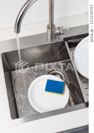 Water running in kitchen sink with dirty dishes and sponge 131556707