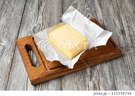 Stick of butter wrapped in foil on wooden cutting board 131556744