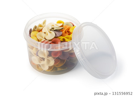 Colorful farfalle pasta stored in open plastic container on white background 131556952