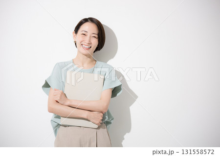 パソコン持つオフィスカジュアルで立つカメラ目線の美人な女性のビジネスイメージ上半身、白背景 笑顔 131558572