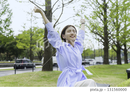 オフィス街の公園で座ってストレッチをする若いビジネスウーマンのポートレート オフィス街の公園で座ってストレッチをする若いビジネスウーマンのポートレート 131560000