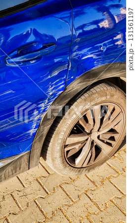 A close-up view of a blue car with visible scratches on the side. The tyre is flat, and the surface shows signs of wear and damage. A close-up view of a blue car with visible scratches on the side. The tyre is flat, and the surface shows signs of wear and damage. 131561197