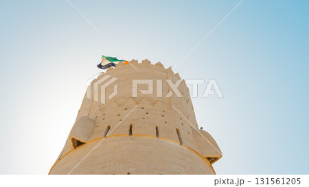 Stone arabic watchtower with waving United Arab Emirates National Flag in Al Jazirah Al Hamra haunted town in Ras Al Khaimah. High quality photo 131561205