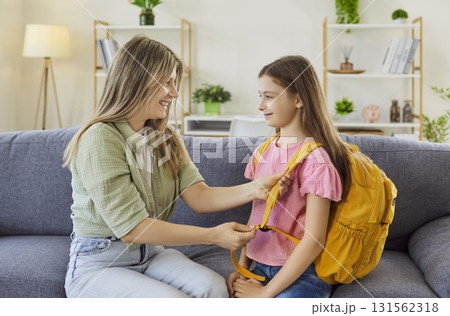 Mother helping daughter with yellow backpack at home before school morning Mother helping daughter with yellow backpack at home before school morning 131562318