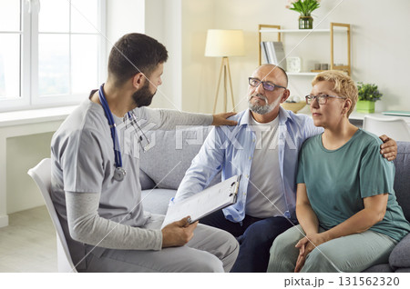 Male nurse comforting senior couple at home during a compassionate medical visit Male nurse comforting senior couple at home during a compassionate medical visit 131562320