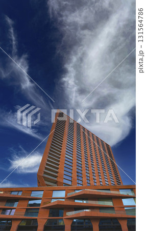 Low-angle view of a contemporary high-rise with a warm terracotta facade and striking, zigzag balconies. 131564786