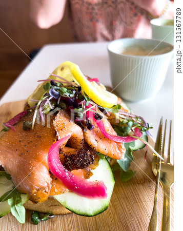 Close up of smoked salmon toast garnished with lemon wedges, cucumber slices, and vibrant microgreens. The fresh toppings highlight a healthy meal option. Close up of smoked salmon toast garnished with lemon wedges, cucumber slices, and vibrant microgreens. The fresh toppings highlight a healthy meal option. 131567789
