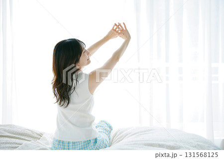 ベッドに座って伸びをする女性 131568125