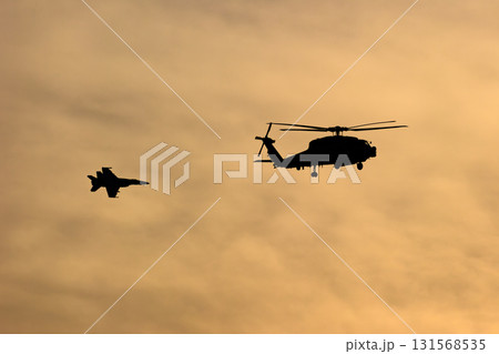夕焼けの空を飛ぶ戦闘機とヘリコプター 131568535