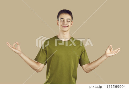 Happy boy in casual clothes doing yoga exercise and meditating isolated on beige background. 131569904